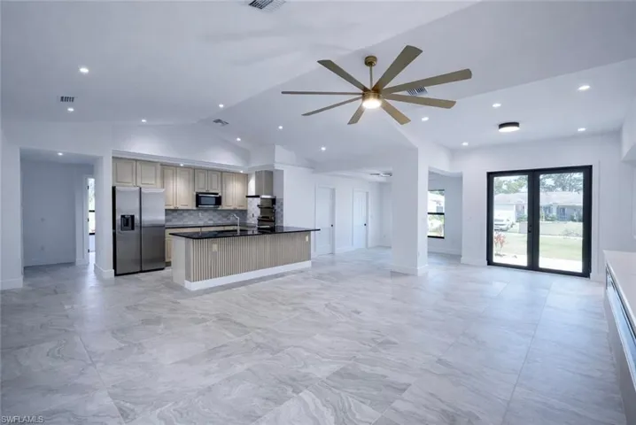 Kitchen featuring open floor plan, stainless steel fridge with ice dispenser, vaulted ceiling, french doors, and tasteful backsplash