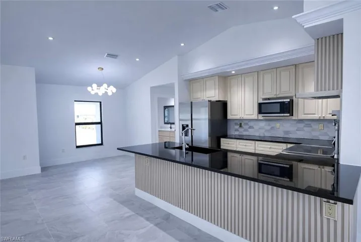 Kitchen with vaulted ceiling, a peninsula, stainless steel appliances, decorative backsplash, and hanging lights