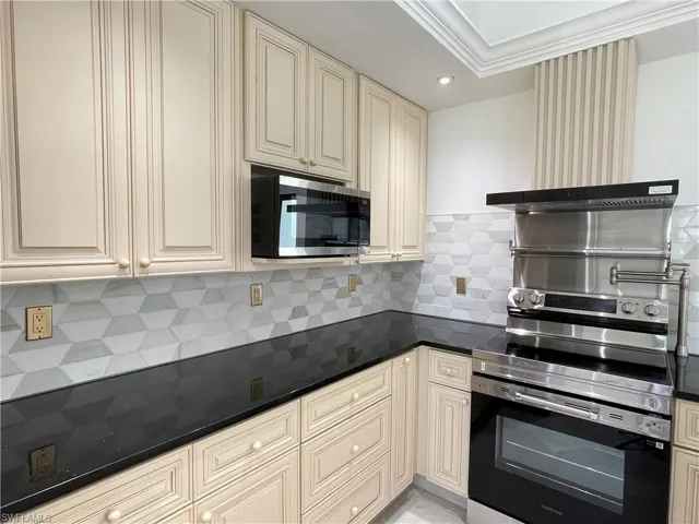 Kitchen featuring cream cabinetry, stainless steel appliances, backsplash, dark stone counters, and recessed lighting
