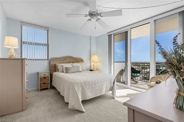Bedroom with light carpet, access to exterior, expansive windows, and a textured ceiling