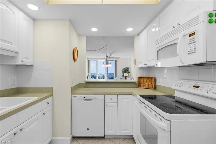 Kitchen with light tile patterned flooring, white appliances, white cabinetry, and light countertops