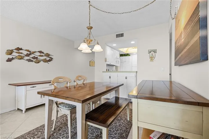 Dining area with a textured ceiling, visible vents, a notable chandelier, and light tile patterned floors