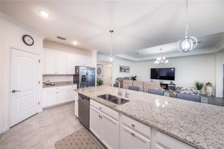 Kitchen island with light stone counters, decorative light fixtures, stainless steel appliances, white cabinets, and sink