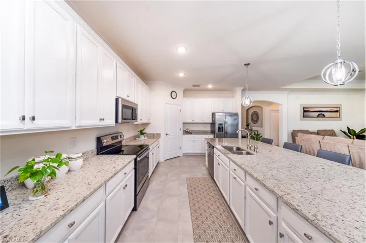 Kitchen featuring white cabinets, stainless steel appliances, hanging light fixtures, light stone countertops, and sink