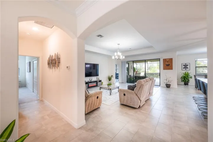 Tiled living room with a raised tray ceiling, a notable chandelier, and crown molding