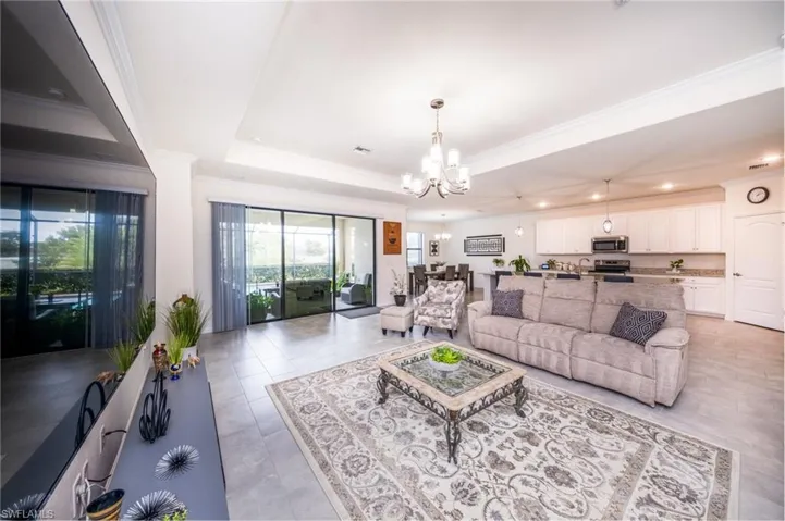 Living room with ornamental molding, light tile flooring, a tray ceiling, and a chandelier