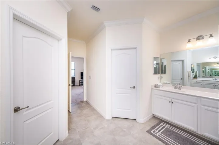 Master Bathroom featuring his and her walk-in closets, crown molding, tile flooring, and dual vanities