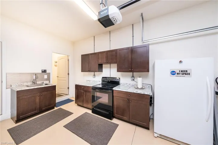 Garage Kitchen featuring white fridge, black electric range, light epoxy floors, sink, and dark brown cabinets