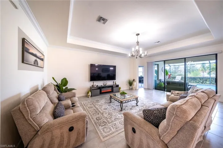 Living room with a notable chandelier, crown molding, a raised tray ceiling, and light tile floors
