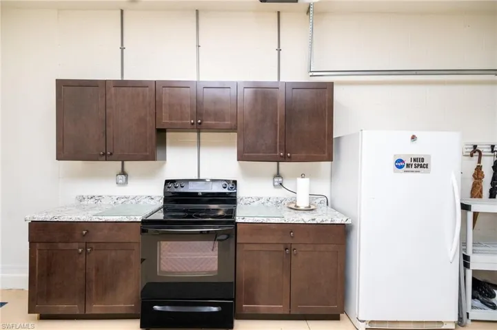 Kitchen with light stone counters, white refrigerator, black electric range, and dark brown cabinets
