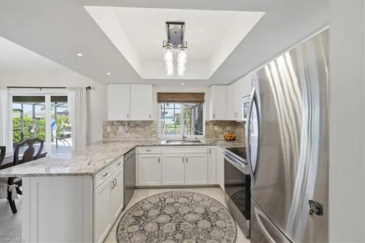 Kitchen with stainless steel appliances, light stone countertops, white cabinets, a peninsula, and a raised ceiling