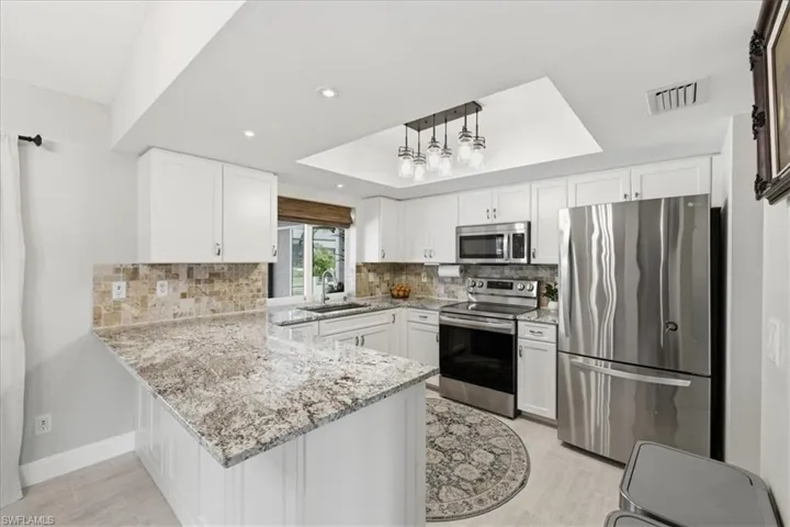 Kitchen with a tray ceiling, stainless steel appliances, a peninsula, light stone counters, and backsplash