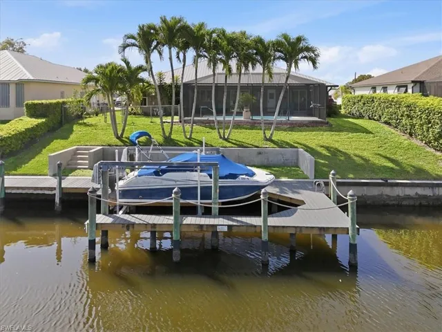 Dock with boat lift, a water view, a sunroom, a yard, and glass enclosure