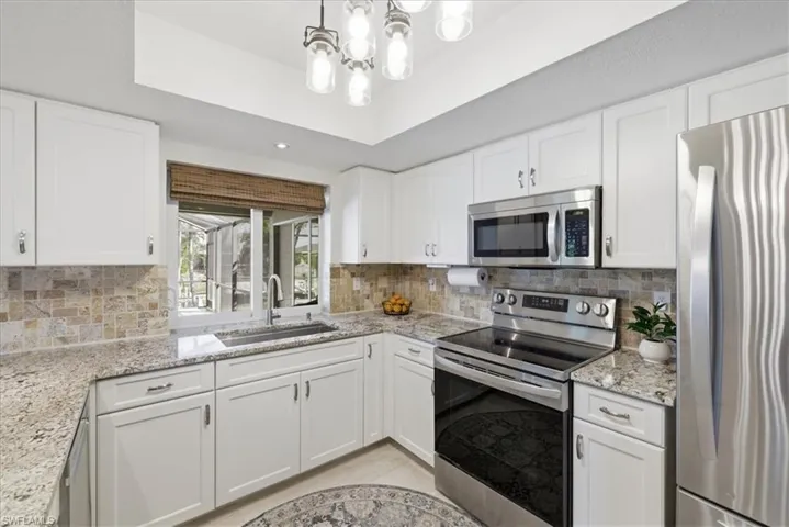 Kitchen with stainless steel appliances, white cabinets, light stone counters, hanging lights, and a raised ceiling