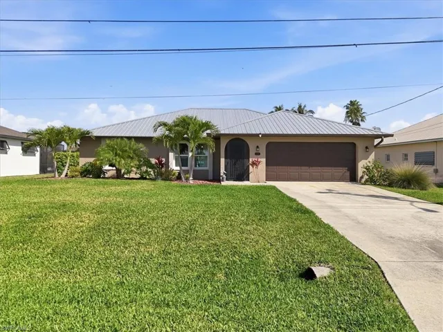 Ranch-style house featuring stucco siding, an attached garage, concrete driveway, a front lawn, and a metal roof