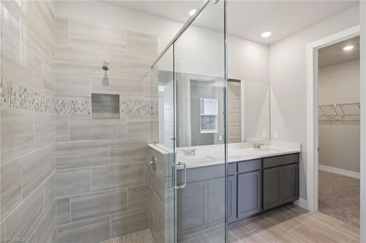 Bathroom featuring a stall shower, double vanity, a spacious closet, and recessed lighting