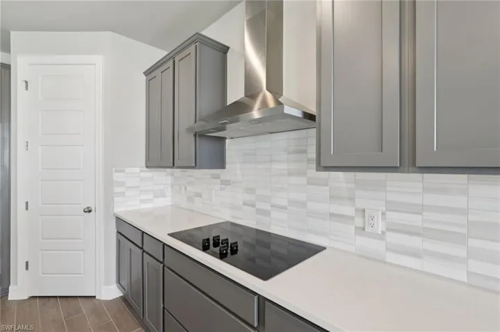 Kitchen with wall chimney range hood, gray cabinets, decorative backsplash, black electric stovetop, and light countertops