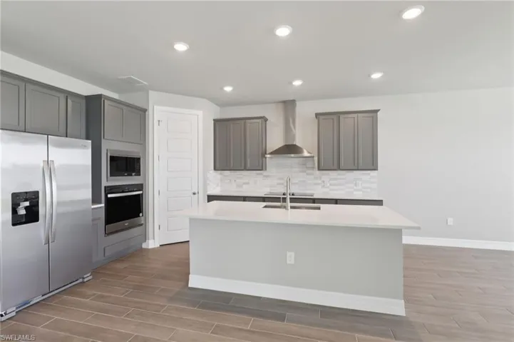 Kitchen with appliances with stainless steel finishes, a center island with sink, wood finished floors, light countertops, and recessed lighting
