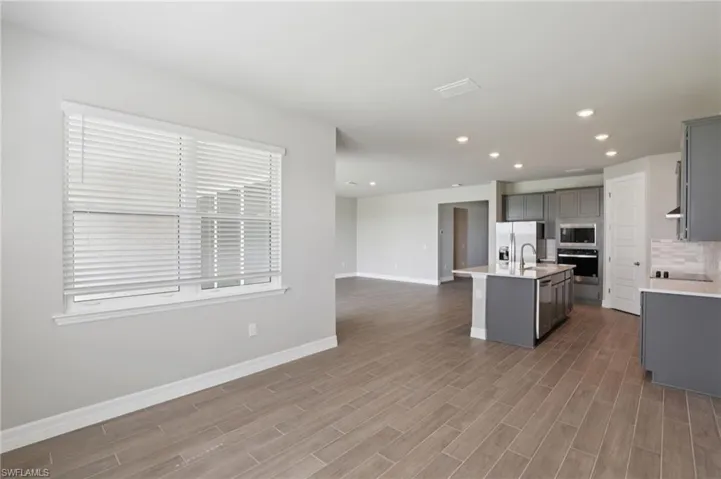 Kitchen with gray cabinets, open floor plan, light countertops, a center island with sink, and appliances with stainless steel finishes