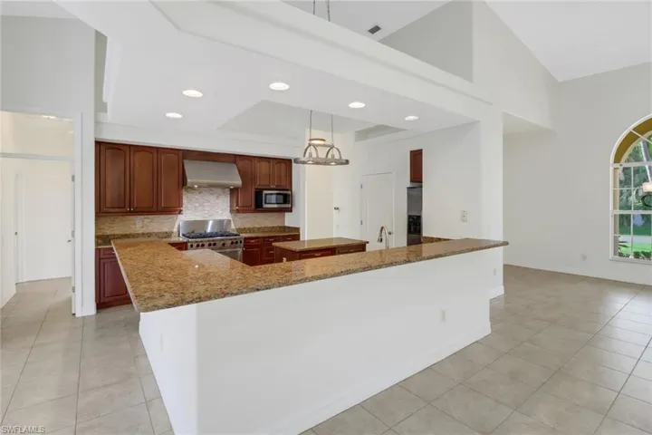 Kitchen featuring appliances with stainless steel finishes, wall chimney exhaust hood, tasteful backsplash, light tile patterned floors, and dark stone countertops