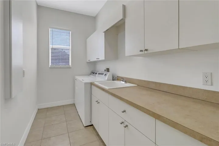 Clothes washing area with sink, washing machine and clothes dryer, cabinets, and light tile patterned floors