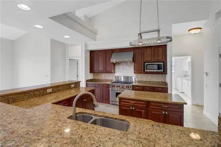 Kitchen with wall chimney exhaust hood, washing machine and dryer, appliances with stainless steel finishes, light tile patterned floors, and sink