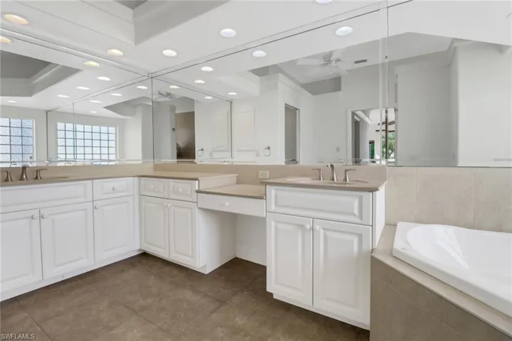 Bathroom with vanity, a raised ceiling, tile patterned floors, a relaxing tiled tub, and ceiling fan