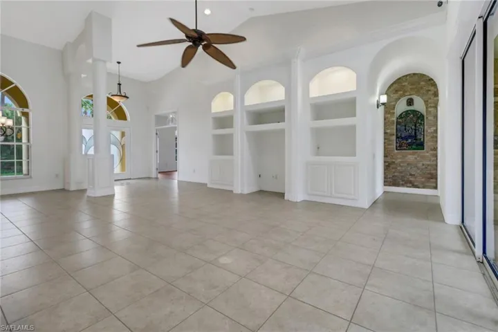 Unfurnished living room with built in features, lofted ceiling, light tile patterned flooring, and ceiling fan