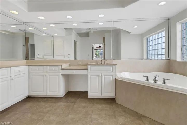 Bathroom with ceiling fan, tiled bath, tile patterned flooring, and vanity