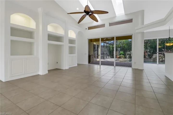 Unfurnished living room featuring ceiling fan, built in shelves, high vaulted ceiling, and light tile patterned flooring