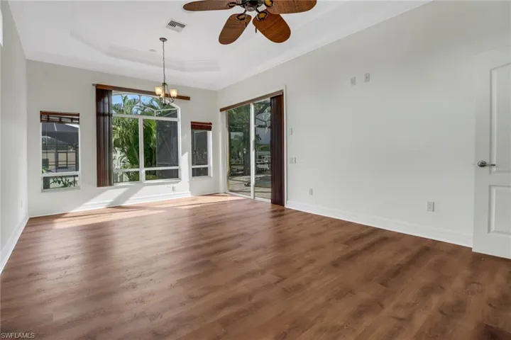 Spare room with a raised ceiling, ceiling fan with notable chandelier, dark wood-type flooring, and crown molding