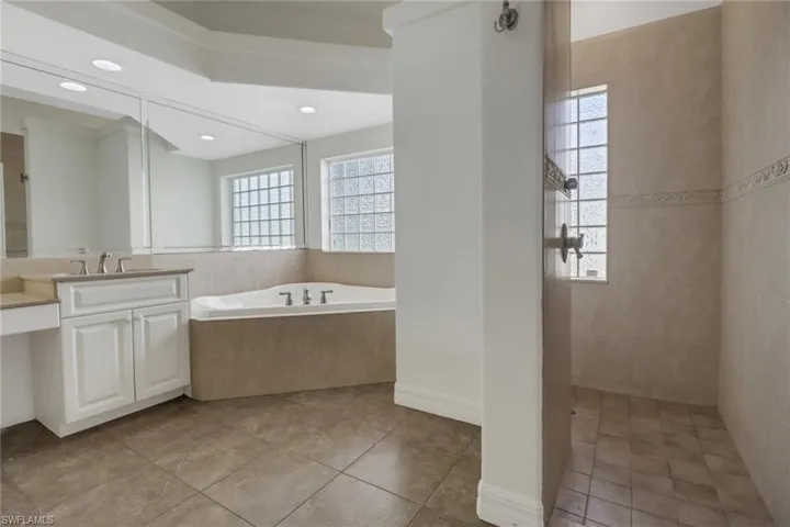 Bathroom featuring tiled tub, a healthy amount of sunlight, vanity, and tile patterned floors