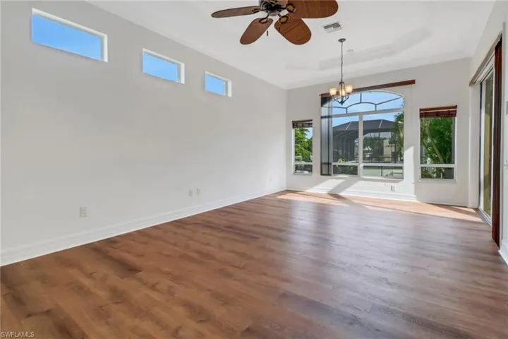 Unfurnished room featuring hardwood / wood-style floors, ceiling fan with notable chandelier, and a tray ceiling