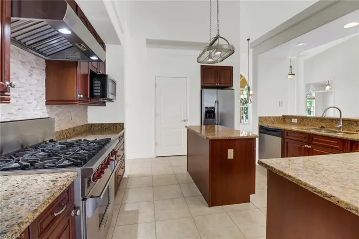 Kitchen featuring stainless steel appliances, wall chimney exhaust hood, sink, light stone counters, and light tile patterned floors