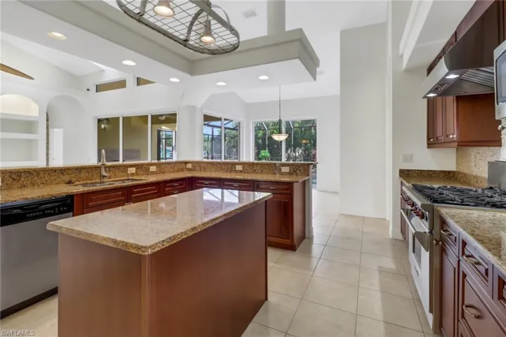 Kitchen with wall chimney exhaust hood, dishwasher, high end range, decorative light fixtures, and a center island