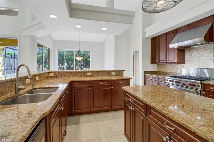Kitchen with wall chimney range hood, backsplash, light stone countertops, luxury range, and sink