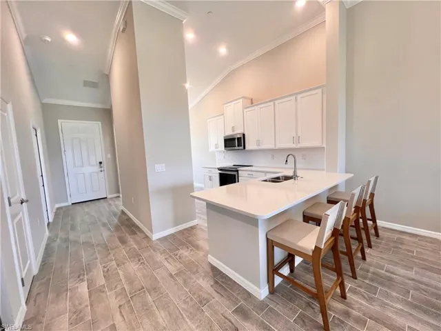 Kitchen with appliances with stainless steel finishes, a breakfast bar, sink, white cabinets, and light hardwood / wood-style floors