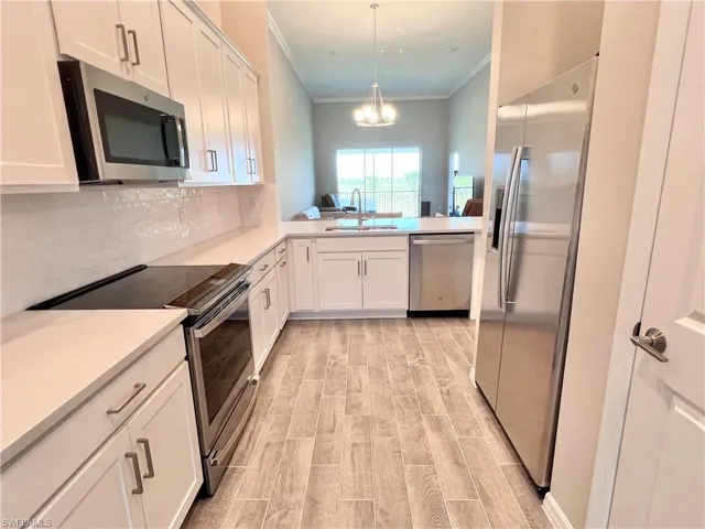 Kitchen featuring pendant lighting, stainless steel appliances, white cabinetry, and sink