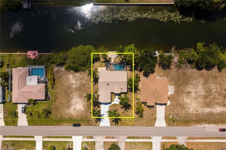 Waterfront property featuring a private swimming pool, mature palm trees, an attached two-car garage, and a concrete driveway