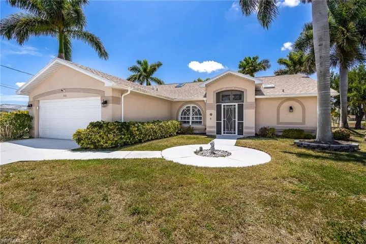 Single-story residence featuring a stucco exterior, an arched entryway, an integrated two-car garage, mature palm trees, and a circular front walkway with a central accent
