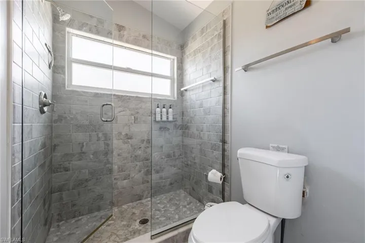 Glass-enclosed shower featuring gray subway tile walls and a pebble-finish floor