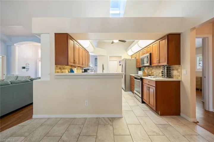 Kitchen featuring warm wood cabinetry, stainless steel appliances, a tiled backsplash, and light-colored countertops
