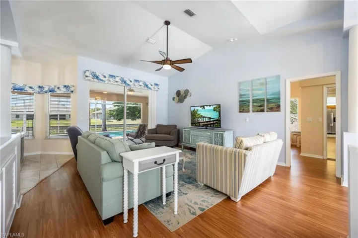 Spacious living area featuring a vaulted ceiling with a ceiling fan, sliding glass doors opening to an outdoor pool, and wood-finish flooring
