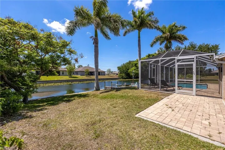 Expansive outdoor living area featuring a screened pool enclosure, paved patio, and canal frontage with a dock