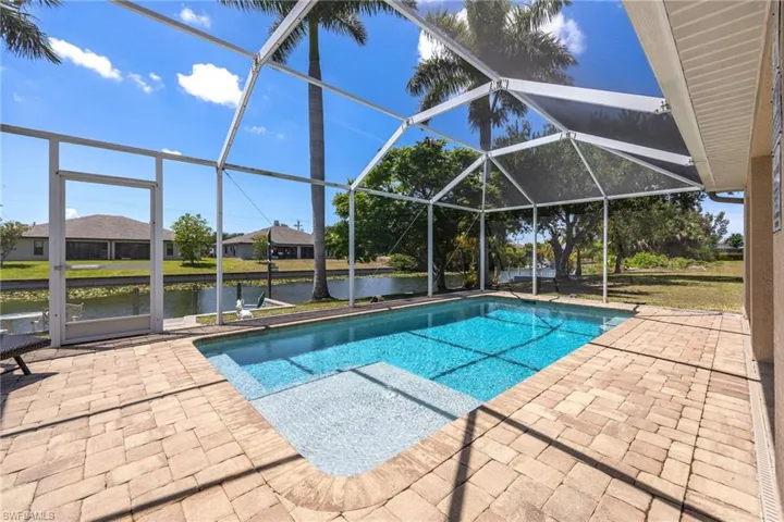 Screened outdoor pool area featuring a rectangular pool with an integrated sun shelf, surrounded by paver decking, and a canal with a dock