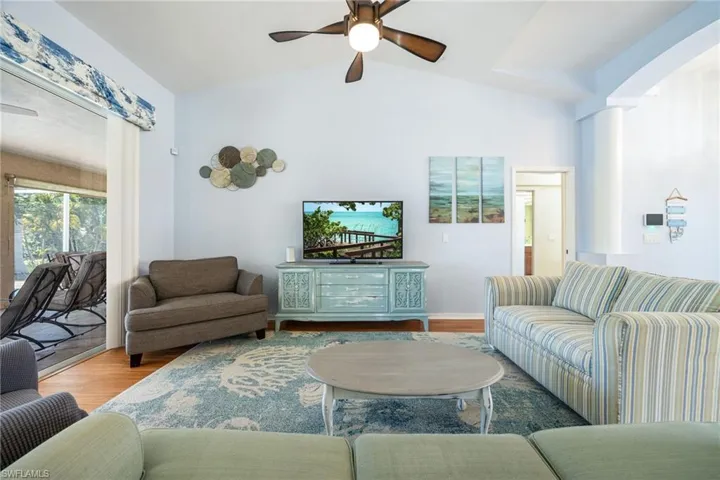 Spacious living area featuring vaulted ceilings, wood-finish flooring, a ceiling fan, and large sliding glass doors leading to an exterior screened patio