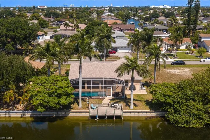 Waterfront residence featuring a private dock, screened pool enclosure, paved patio, and mature palm trees