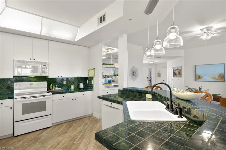 Kitchen with white appliances, sink, hanging light fixtures, white cabinetry, and ceiling fan