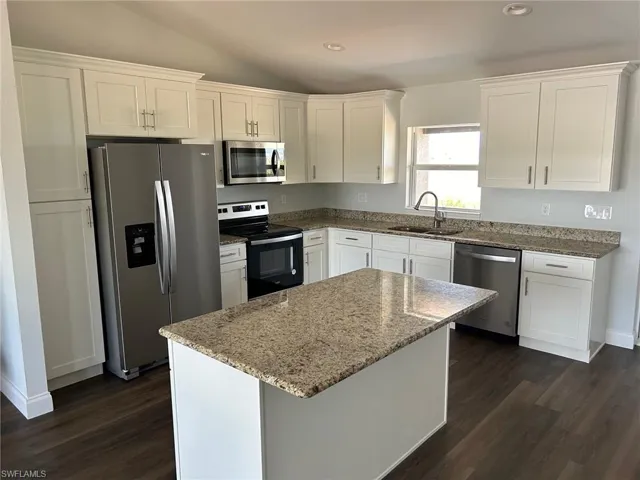 Kitchen with dark hardwood / wood-style floors, stainless steel appliances, white cabinets, and sink