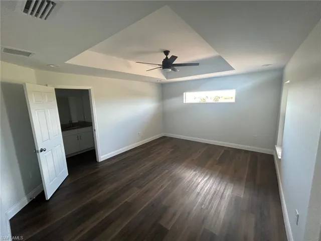 Unfurnished bedroom featuring a raised ceiling, ceiling fan, and dark hardwood / wood-style floors
